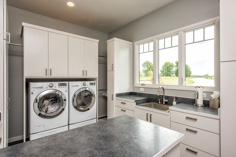 Foto di una grande sala lavanderia contemporanea con lavatrice e asciugatrice affiancate, lavello a vasca singola, ante lisce, ante bianche, pareti grigie e top grigio