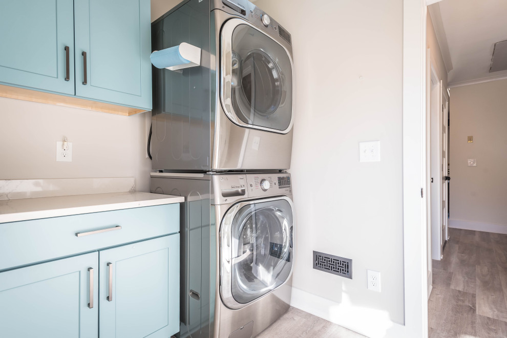 Idee per una piccola lavanderia minimalista con ante con riquadro incassato, ante blu, paraspruzzi beige, pareti beige, parquet chiaro, lavatrice e asciugatrice a colonna, pavimento beige e top bianco