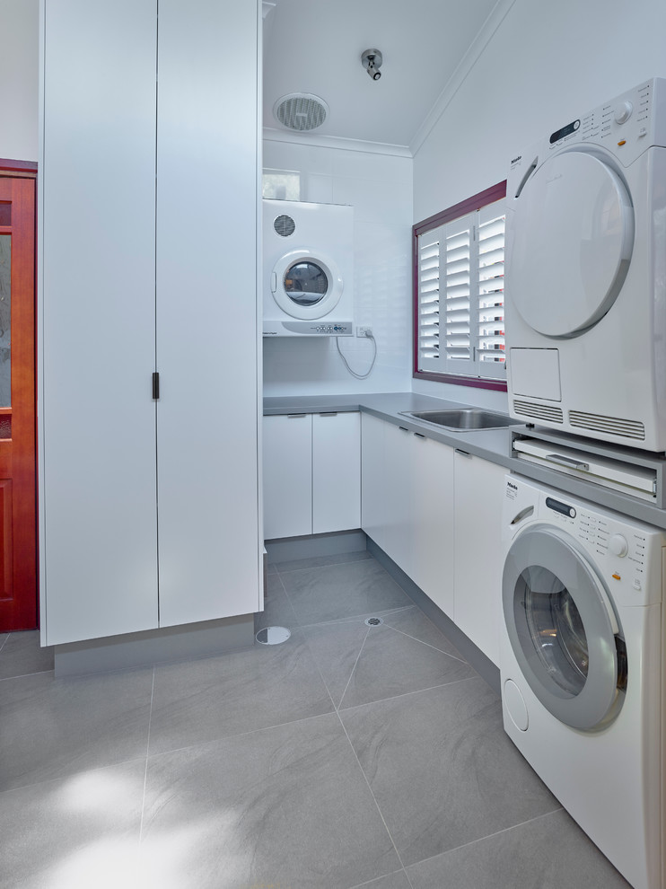 Immagine di una sala lavanderia minimal di medie dimensioni con lavello da incasso, ante bianche, top in laminato, pareti bianche e lavatrice e asciugatrice a colonna