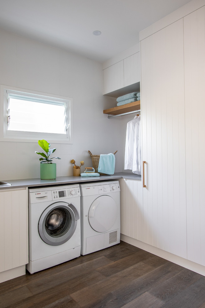 Inspiration för moderna u-formade grått tvättstugor, med vita skåp, bänkskiva i kvarts, vita väggar, mellanmörkt trägolv och en tvättmaskin och torktumlare bredvid varandra