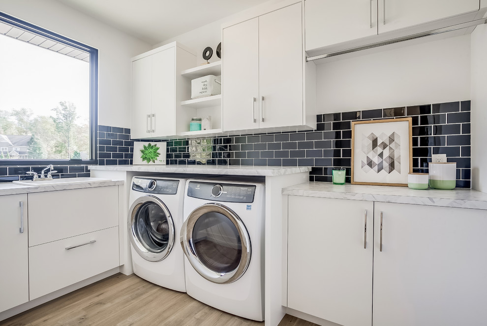 グランドラピッズにあるコンテンポラリースタイルのおしゃれな洗濯室 (L型、ドロップインシンク、フラットパネル扉のキャビネット、白いキャビネット、白い壁、淡色無垢フローリング、左右配置の洗濯機・乾燥機) の写真