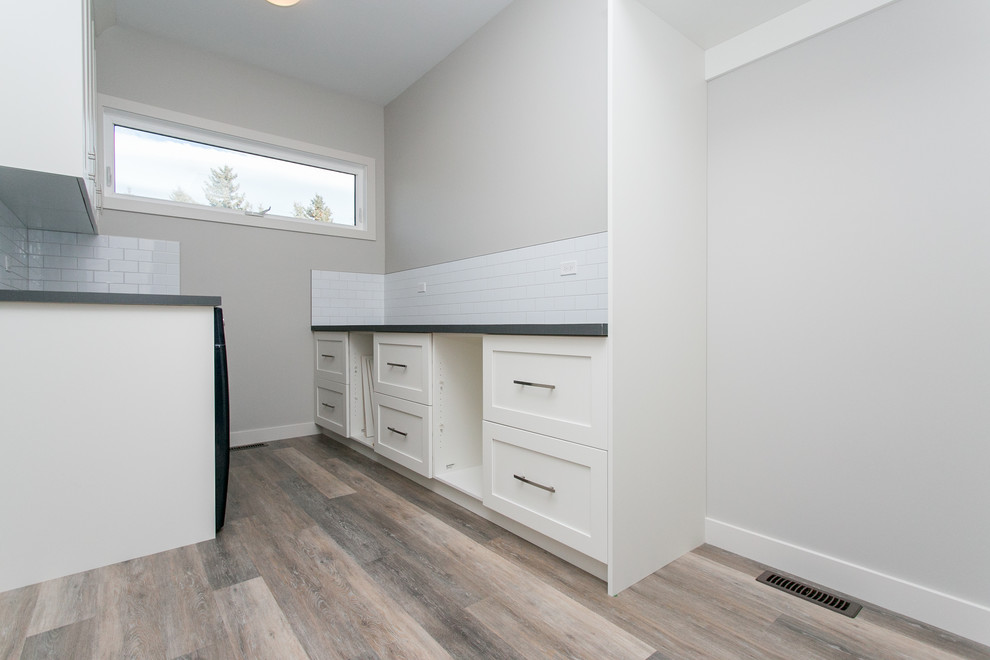 Mittelgroße Klassische Waschküche in U-Form mit Schrankfronten im Shaker-Stil, weißen Schränken, weißer Wandfarbe, braunem Holzboden und Waschmaschine und Trockner nebeneinander in Calgary