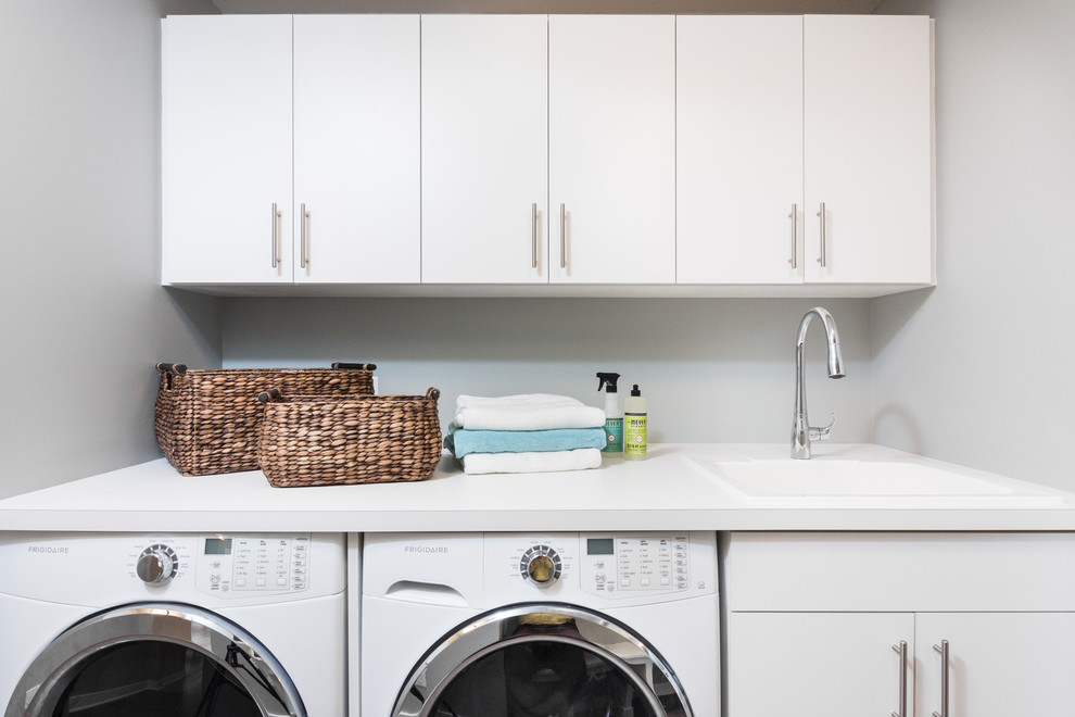 Esempio di una lavanderia multiuso minimal di medie dimensioni con lavello da incasso, ante lisce, ante bianche, top in laminato, pareti grigie, lavatrice e asciugatrice affiancate e pavimento grigio