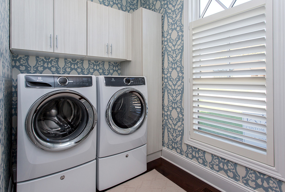 Lantlig inredning av en liten parallell tvättstuga enbart för tvätt, med släta luckor, skåp i ljust trä, blå väggar, mellanmörkt trägolv, en tvättmaskin och torktumlare bredvid varandra och brunt golv