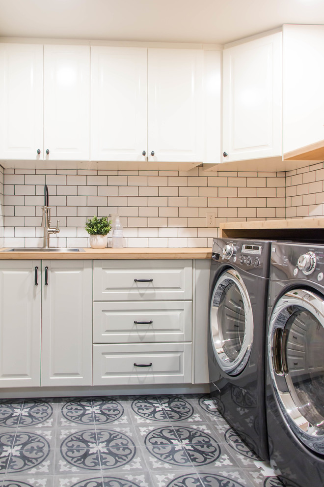 This is an example of a medium sized farmhouse l-shaped separated utility room in Calgary with a built-in sink, white cabinets, wood worktops, grey walls, porcelain flooring, a side by side washer and dryer, grey floors and raised-panel cabinets.
