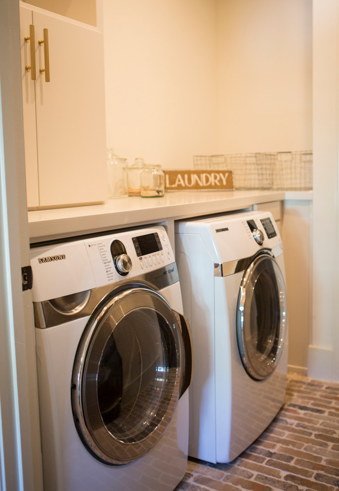 アトランタにある高級な広いカントリー風のおしゃれな洗濯室 (I型、フラットパネル扉のキャビネット、白いキャビネット、人工大理石カウンター、白い壁、レンガの床、左右配置の洗濯機・乾燥機) の写真
