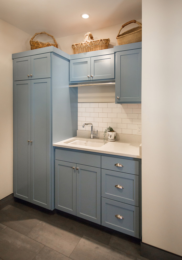 Bild på en lantlig linjär tvättstuga, med en undermonterad diskho, skåp i shakerstil, blå skåp, bänkskiva i kvarts, beige väggar, klinkergolv i porslin och grått golv