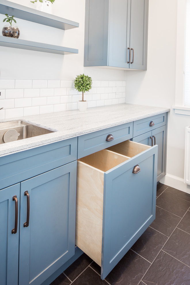 Example of a small farmhouse galley porcelain tile and gray floor utility room design in Vancouver with an undermount sink, shaker cabinets, blue cabinets, solid surface countertops, gray walls, a side-by-side washer/dryer and gray countertops