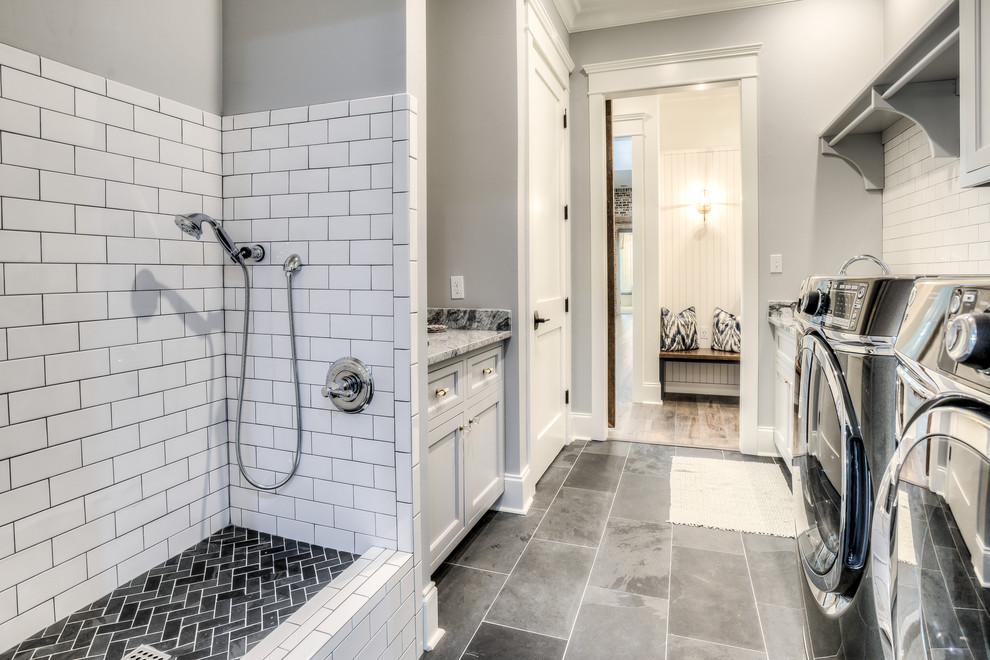 Exempel på en mellanstor lantlig parallell tvättstuga, med en undermonterad diskho, luckor med profilerade fronter, grå skåp, granitbänkskiva, grå väggar, en tvättmaskin och torktumlare bredvid varandra och grått golv