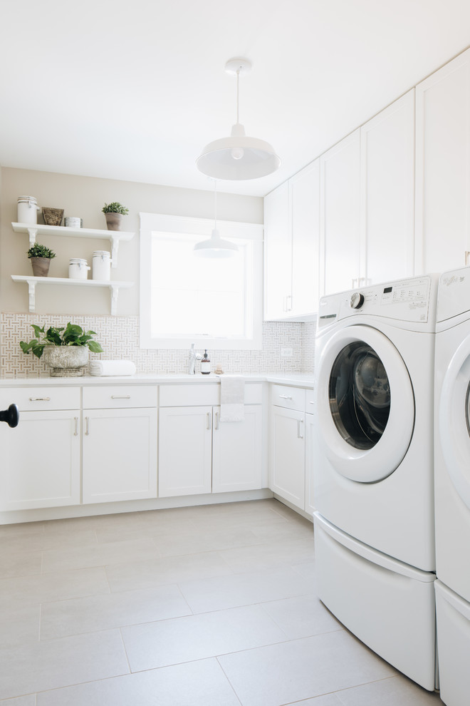 Diseño de lavadero en L de estilo de casa de campo con armarios estilo shaker, puertas de armario blancas, paredes beige, lavadora y secadora juntas y suelo gris