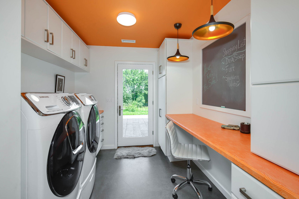 プロビデンスにあるお手頃価格の中くらいなインダストリアルスタイルのおしゃれな家事室 (ll型、スロップシンク、フラットパネル扉のキャビネット、白いキャビネット、ラミネートカウンター、オレンジの壁、コンクリートの床、左右配置の洗濯機・乾燥機、グレーの床、オレンジのキッチンカウンター) の写真