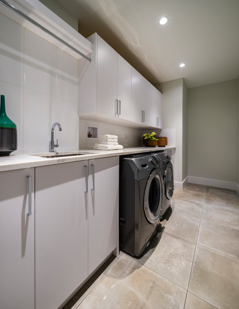 Design ideas for a large contemporary single-wall separated utility room in Vancouver with a submerged sink, flat-panel cabinets, white cabinets, engineered stone countertops, grey walls, porcelain flooring, a side by side washer and dryer, grey floors and grey worktops.