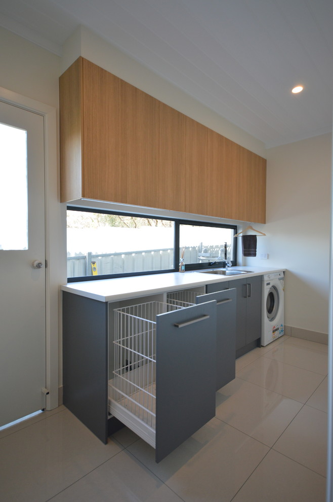 Idee per una sala lavanderia moderna di medie dimensioni con ante in legno chiaro, top in laminato, pareti bianche e pavimento in gres porcellanato