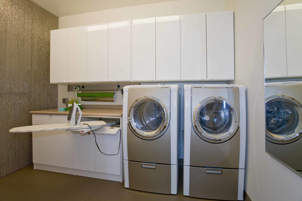 ポートランドにある高級な中くらいなコンテンポラリースタイルのおしゃれな家事室 (ll型、フラットパネル扉のキャビネット、白いキャビネット、左右配置の洗濯機・乾燥機、グレーの壁) の写真