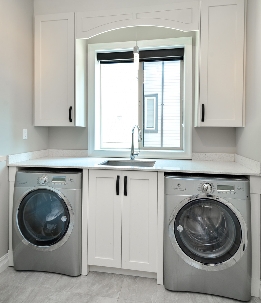 Immagine di una lavanderia minimalista con lavello sottopiano, lavatrice e asciugatrice affiancate, ante in stile shaker, ante bianche, top in quarzite e pareti grigie