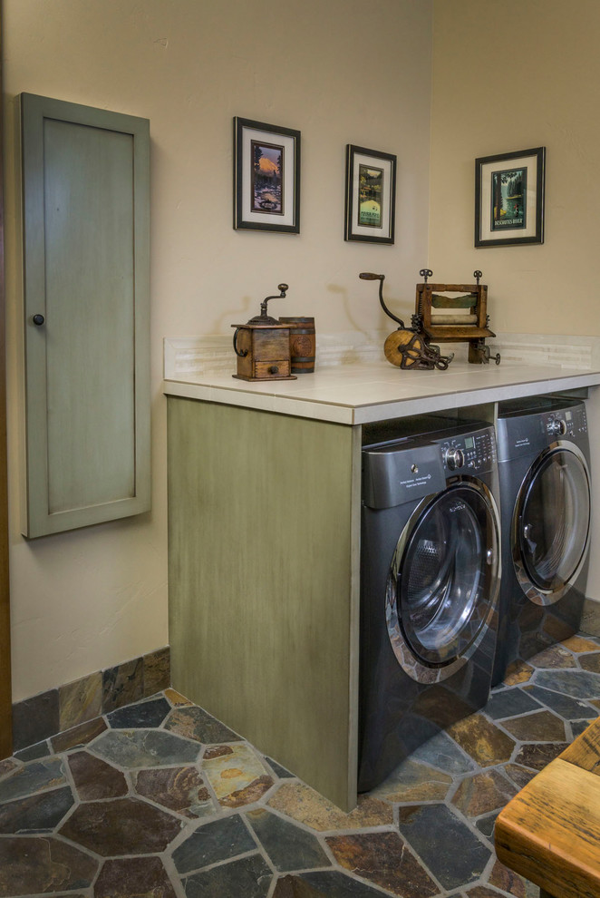 Exempel på en stor lantlig beige u-formad beige tvättstuga enbart för tvätt, med en rustik diskho, skåp i shakerstil, gröna skåp, bänkskiva i kvarts, beige väggar, en tvättmaskin och torktumlare bredvid varandra och flerfärgat golv