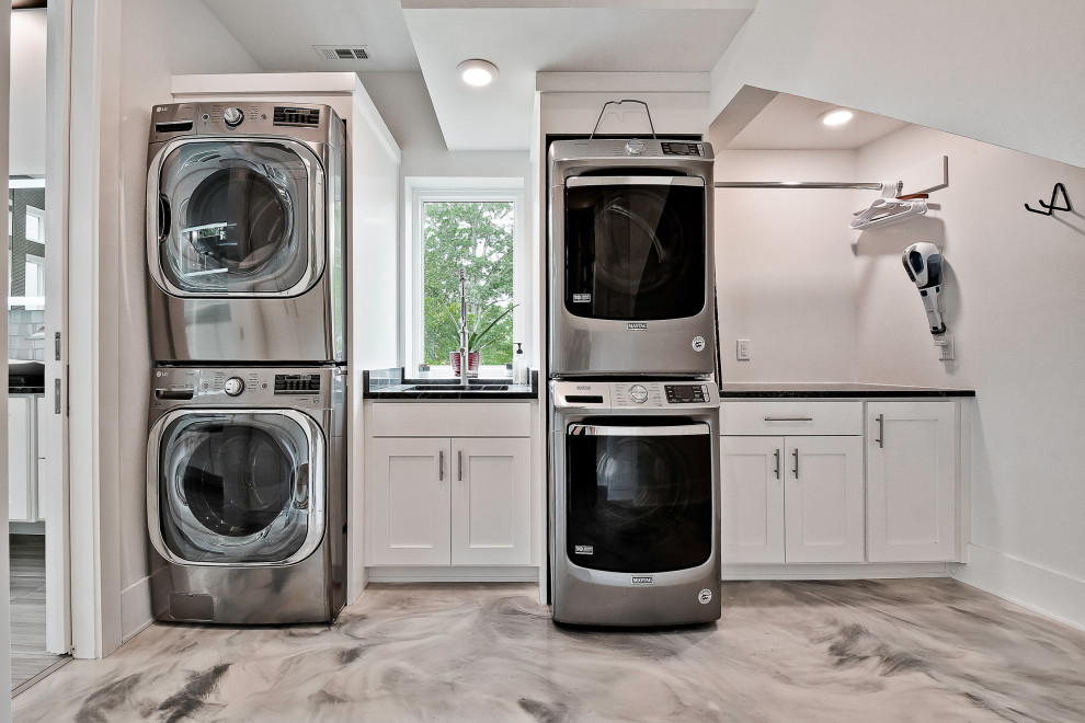 Example of a mid-sized minimalist concrete floor and gray floor dedicated laundry room design in Other with an undermount sink, granite countertops, white walls, a stacked washer/dryer and black countertops