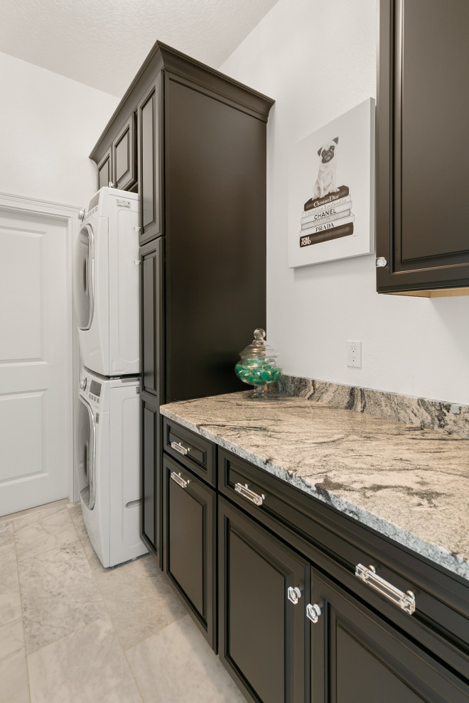 Photo of a small modern single-wall separated utility room in Jacksonville with raised-panel cabinets, brown cabinets, granite worktops, white walls, marble flooring, a stacked washer and dryer, white floors and beige worktops.