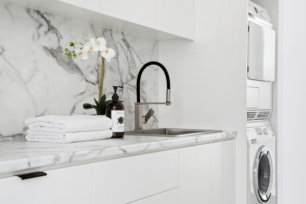 Foto de cuarto de lavado lineal minimalista de tamaño medio con fregadero encastrado, encimera de mármol, lavadora y secadora apiladas y encimeras blancas