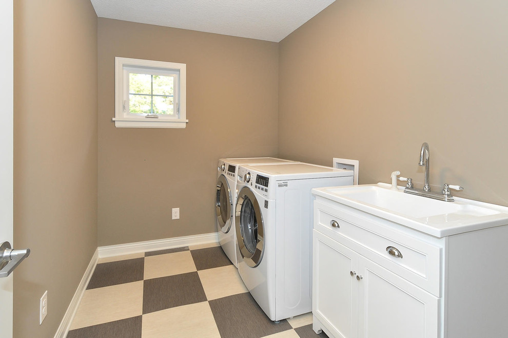 Idéer för en mellanstor klassisk vita linjär tvättstuga enbart för tvätt, med en integrerad diskho, skåp i shakerstil, vita skåp, bänkskiva i kvarts, bruna väggar, vinylgolv, en tvättmaskin och torktumlare bredvid varandra och brunt golv