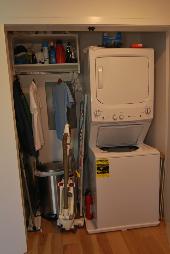 Exempel på en liten modern liten tvättstuga, med släta luckor, vita skåp, mellanmörkt trägolv, en tvättpelare och flerfärgat golv