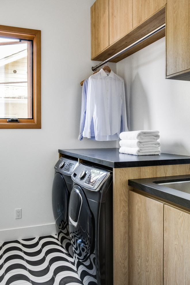 Medium sized contemporary single-wall separated utility room in Orange County with a submerged sink, flat-panel cabinets, light wood cabinets, soapstone worktops, white walls, ceramic flooring, a side by side washer and dryer, multi-coloured floors and black worktops.