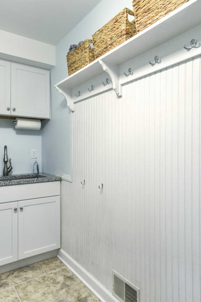 Bild på en mellanstor vintage linjär tvättstuga enbart för tvätt, med en undermonterad diskho, skåp i shakerstil, vita skåp, granitbänkskiva, blå väggar, travertin golv och en tvättpelare