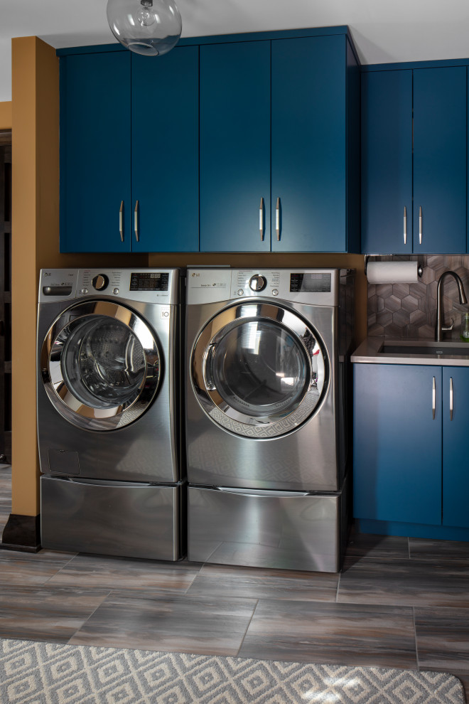 Immagine di una lavanderia multiuso rustica con lavello sottopiano, ante lisce, ante blu, top in quarzo composito, pareti arancioni, pavimento in gres porcellanato, lavatrice e asciugatrice affiancate, pavimento marrone e top grigio