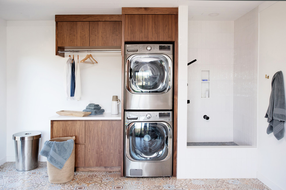 Immagine di una lavanderia multiuso rustica con ante lisce, ante in legno bruno, pareti bianche, lavatrice e asciugatrice a colonna, pavimento multicolore e top bianco