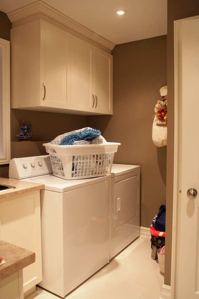 モントリオールにあるお手頃価格の中くらいなコンテンポラリースタイルのおしゃれな洗濯室 (I型、ドロップインシンク、落し込みパネル扉のキャビネット、白いキャビネット、ラミネートカウンター、茶色い壁、セラミックタイルの床、左右配置の洗濯機・乾燥機) の写真