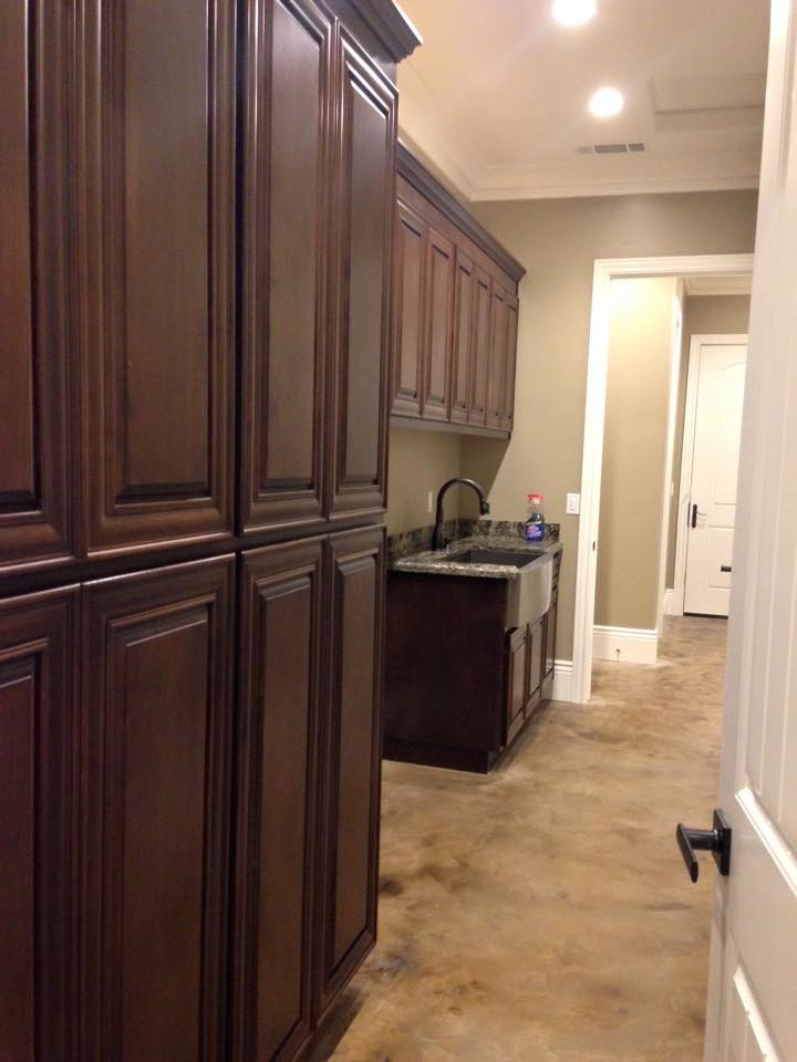 Large traditional galley utility room in Sacramento with a belfast sink, raised-panel cabinets, dark wood cabinets, granite worktops, beige walls, concrete flooring and a side by side washer and dryer.