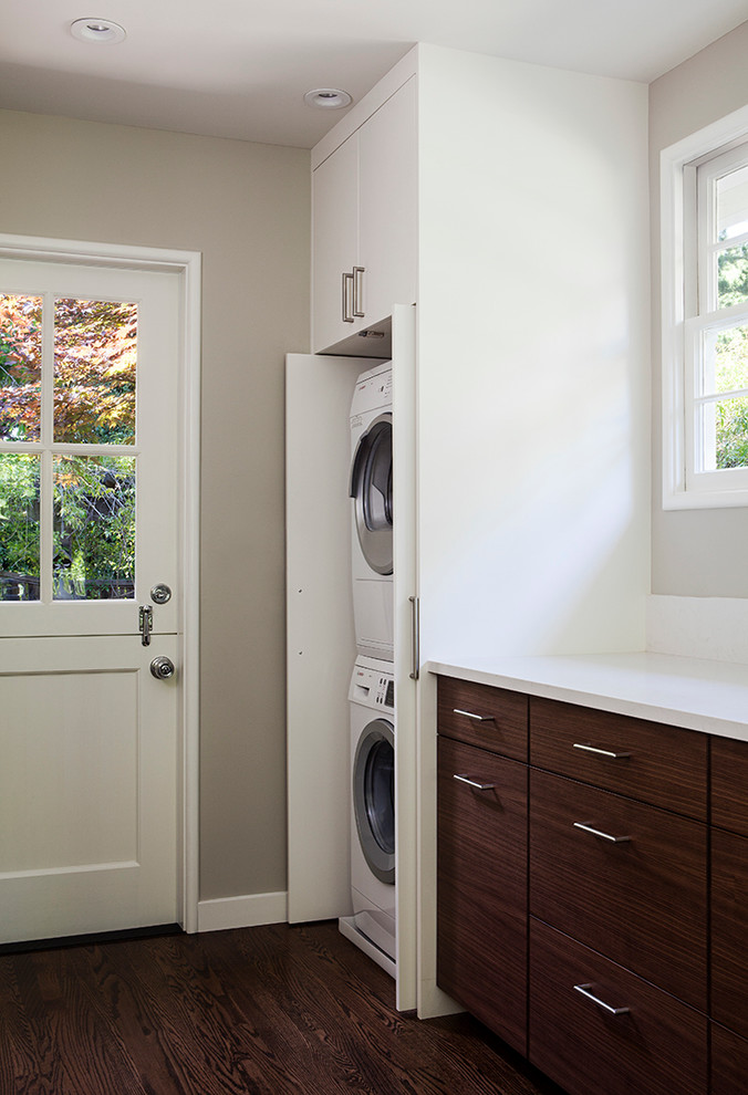 Diseño de armario lavadero lineal contemporáneo pequeño con armarios con paneles lisos, puertas de armario blancas, paredes grises, suelo de madera oscura y lavadora y secadora apiladas