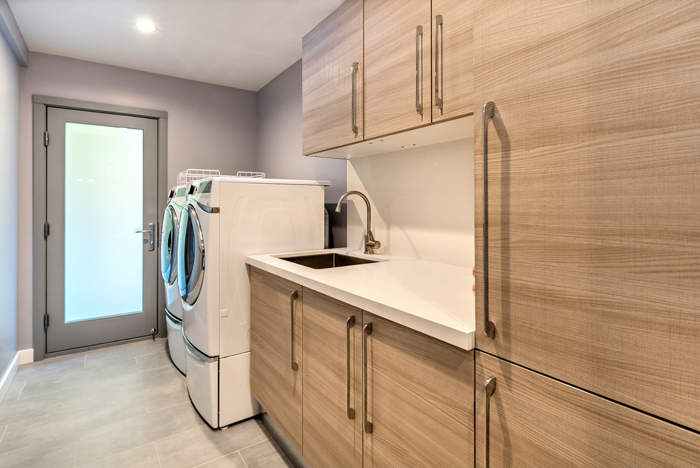 Foto på en mellanstor funkis linjär tvättstuga enbart för tvätt, med en nedsänkt diskho, släta luckor, skåp i ljust trä, bänkskiva i kvarts, grå väggar och en tvättmaskin och torktumlare bredvid varandra
