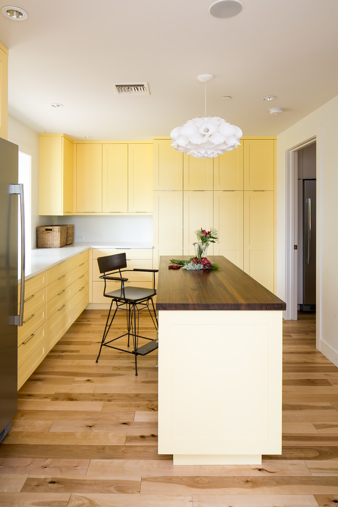 Пример оригинального дизайна: угловая универсальная комната в стиле ретро с желтыми фасадами, столешницей из кварцита, белыми стенами, светлым паркетным полом, со скрытой стиральной машиной, фасадами в стиле шейкер, коричневым полом и белой столешницей