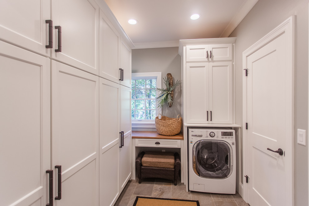 Utility room - mid-sized transitional galley laminate floor and gray floor utility room idea in Cincinnati with raised-panel cabinets, white cabinets, granite countertops, gray walls, a stacked washer/dryer and brown countertops