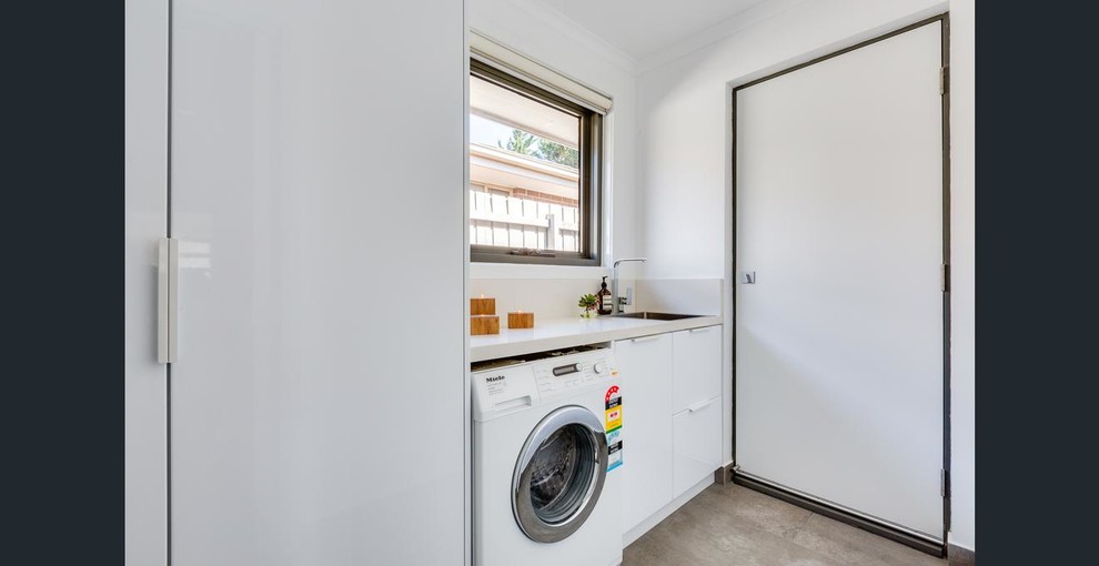 Einzeilige, Kleine Moderne Waschküche mit flächenbündigen Schrankfronten, weißen Schränken, Quarzwerkstein-Arbeitsplatte, weißer Wandfarbe, Porzellan-Bodenfliesen, braunem Boden, weißer Arbeitsplatte und Einbauwaschbecken in Melbourne