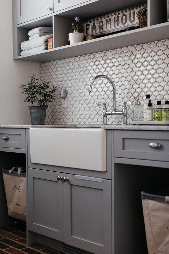 Design ideas for a medium sized rural single-wall separated utility room in Vancouver with a belfast sink, shaker cabinets, grey cabinets, marble worktops, white walls, porcelain flooring, a stacked washer and dryer, brown floors and white worktops.