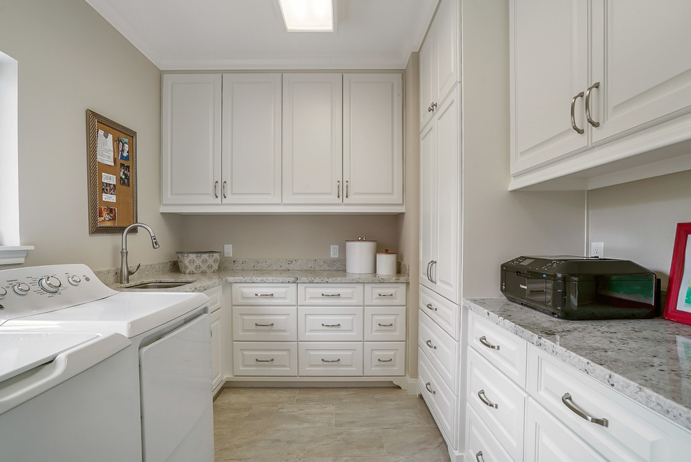 Photo of a traditional u-shaped utility room in Houston with an utility sink, raised-panel cabinets, white cabinets, granite worktops, beige walls, porcelain flooring, a side by side washer and dryer, beige floors and white worktops.