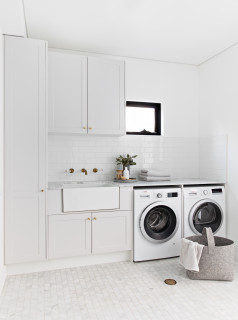 Classic cottage laundry room features a white and gray granite countertop  positioned over a sil…