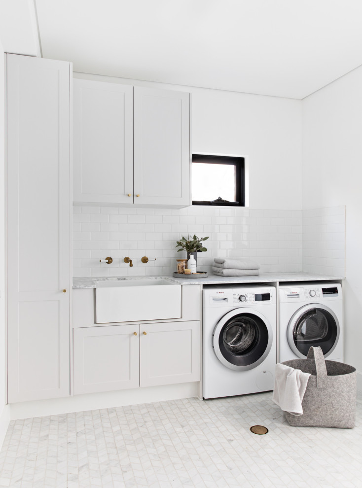 シドニーにある北欧スタイルのおしゃれなランドリールーム (I型、エプロンフロントシンク、シェーカースタイル扉のキャビネット、白いキャビネット、白い壁、大理石の床、左右配置の洗濯機・乾燥機、白い床、グレーのキッチンカウンター) の写真