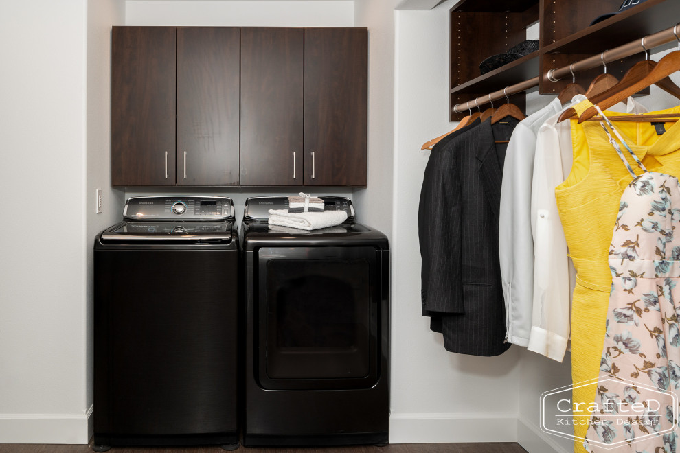 Photo of a medium sized modern laundry cupboard in Seattle with flat-panel cabinets, dark wood cabinets, white walls, vinyl flooring, a side by side washer and dryer and brown floors.