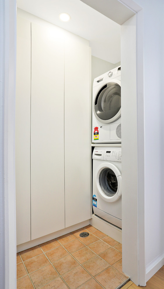 シドニーにある高級な小さな北欧スタイルのおしゃれな洗濯室 (L型、フラットパネル扉のキャビネット、白いキャビネット、ラミネートカウンター、白い壁、磁器タイルの床、オレンジの床、白いキッチンカウンター) の写真