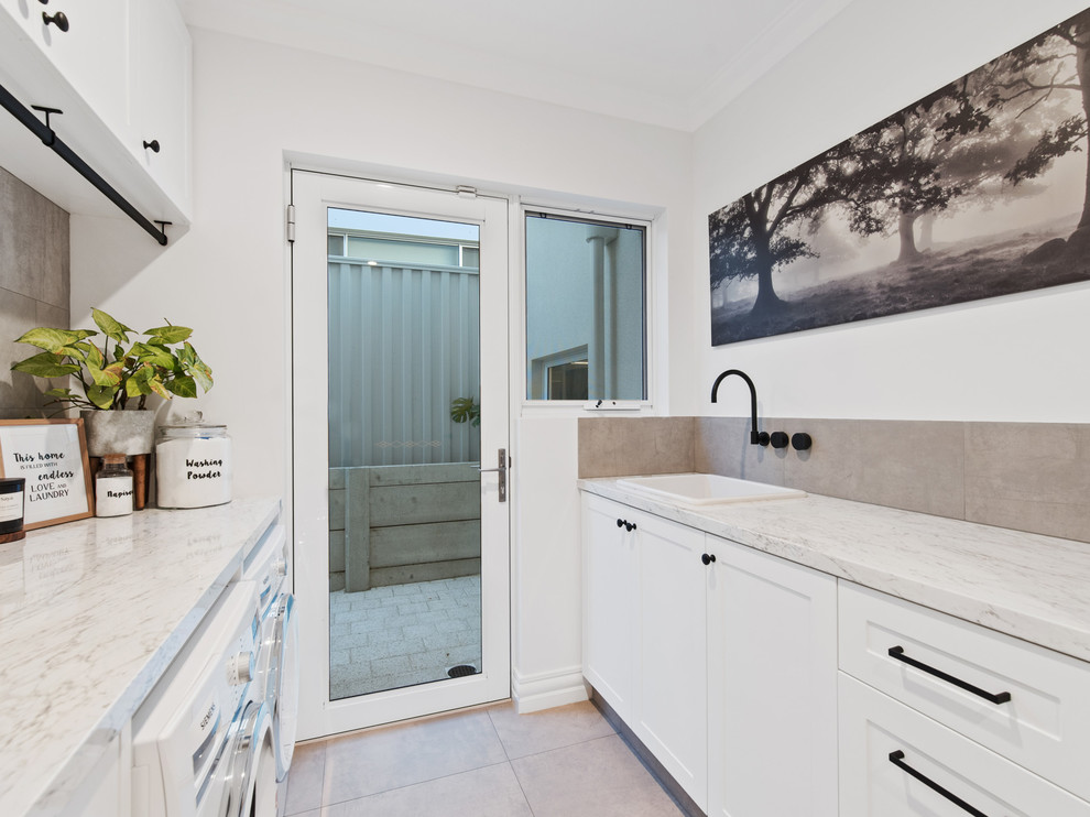 Zweizeiliger Moderner Hauswirtschaftsraum mit Einbauwaschbecken, Schrankfronten im Shaker-Stil, weißen Schränken, weißer Wandfarbe, Waschmaschine und Trockner nebeneinander, beigem Boden und beiger Arbeitsplatte in Perth