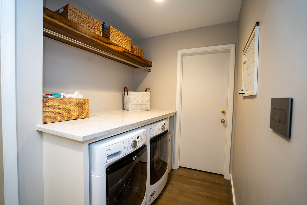 Foto di una piccola sala lavanderia moderna con top in quarzo composito, pareti grigie, pavimento in legno massello medio, lavatrice e asciugatrice affiancate, pavimento marrone e top bianco