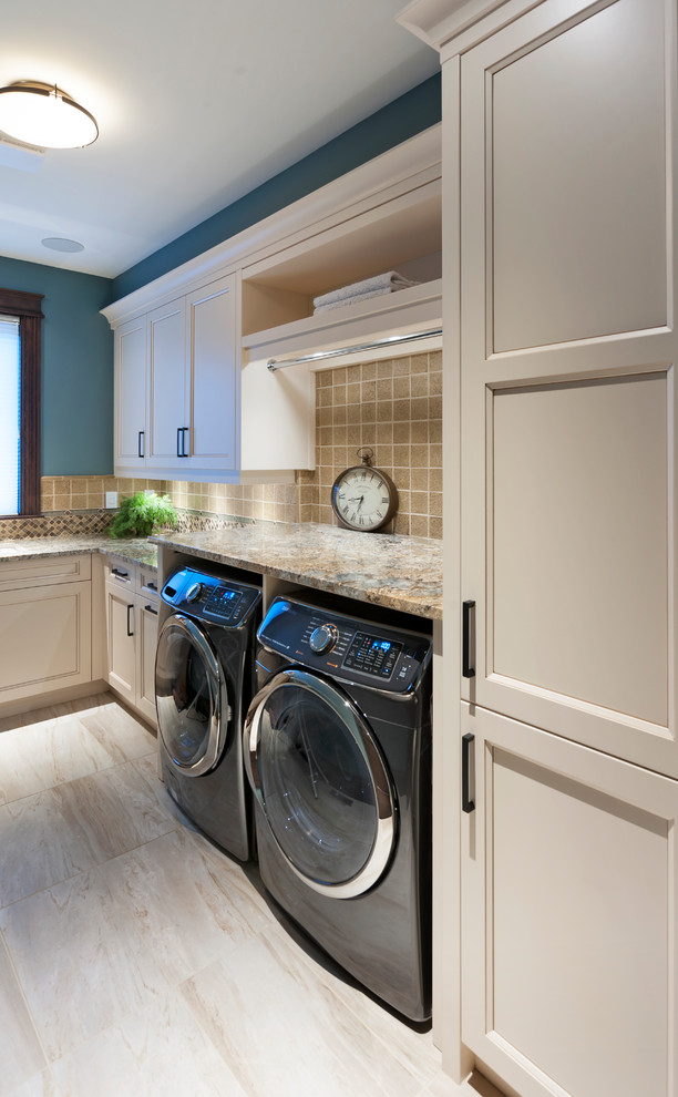 Inredning av en rustik mellanstor l-formad tvättstuga enbart för tvätt, med en undermonterad diskho, skåp i shakerstil, beige skåp, granitbänkskiva, blå väggar, klinkergolv i porslin, en tvättmaskin och torktumlare bredvid varandra och beiget golv