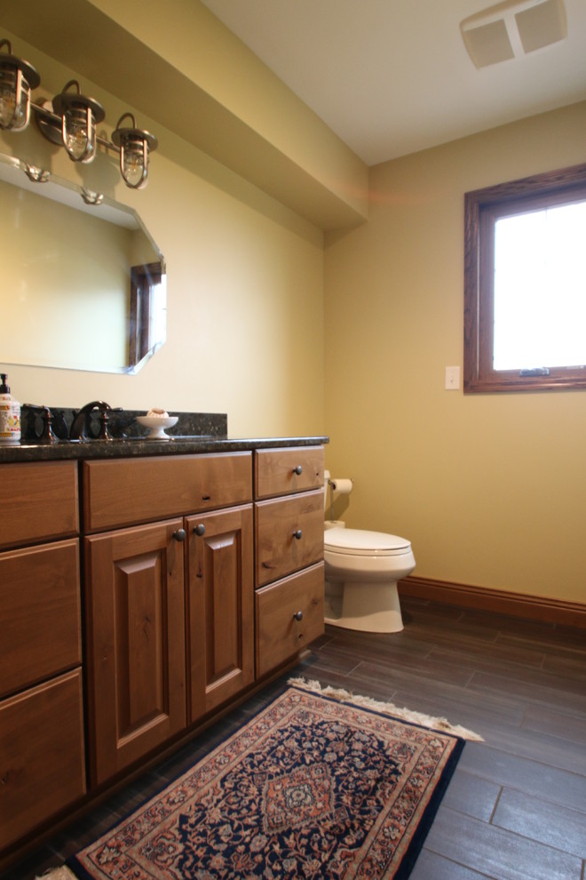 Exempel på ett mellanstort klassiskt l-format grovkök, med en nedsänkt diskho, luckor med upphöjd panel, skåp i mellenmörkt trä, granitbänkskiva, gula väggar, klinkergolv i porslin, en tvättmaskin och torktumlare bredvid varandra och brunt golv