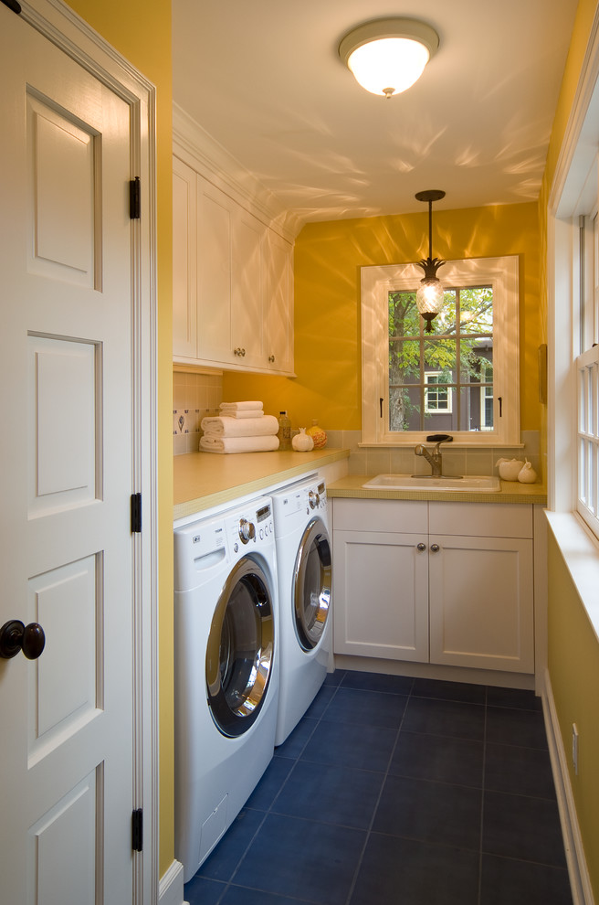 Inspiration för en liten vintage l-formad tvättstuga enbart för tvätt, med en nedsänkt diskho, vita skåp, laminatbänkskiva, gula väggar, en tvättmaskin och torktumlare bredvid varandra, klinkergolv i keramik och skåp i shakerstil