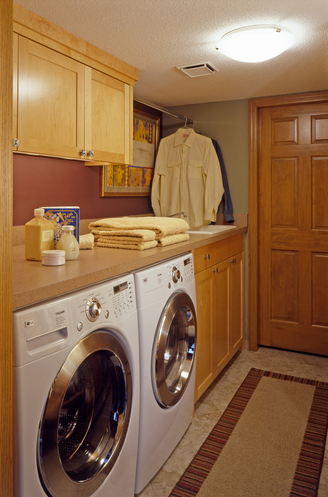 Bild på en liten vintage parallell tvättstuga enbart för tvätt, med en nedsänkt diskho, luckor med infälld panel, laminatbänkskiva, en tvättmaskin och torktumlare bredvid varandra, linoleumgolv, skåp i mellenmörkt trä och gröna väggar