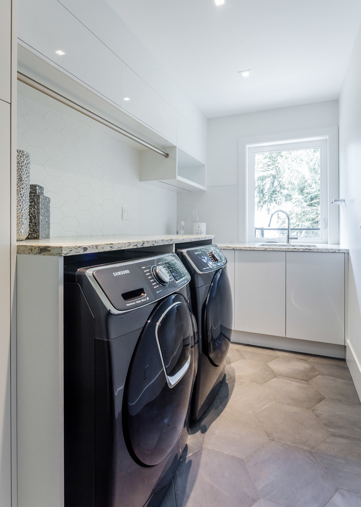 Idee per una lavanderia moderna di medie dimensioni con lavello sottopiano, ante lisce, ante bianche, pareti bianche, pavimento in cemento, lavatrice e asciugatrice affiancate e pavimento grigio