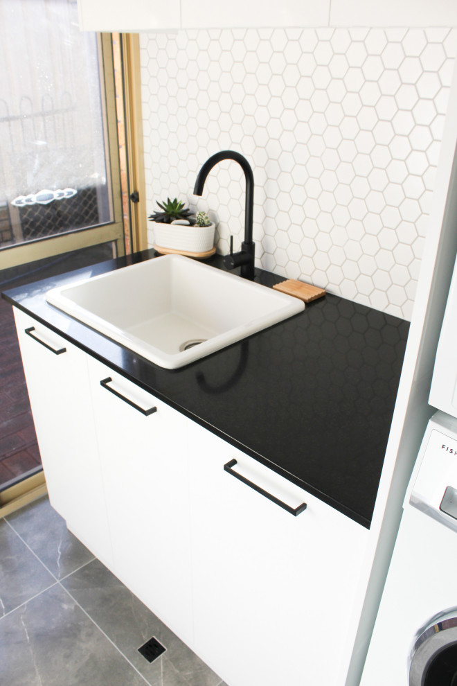 Photo of a small modern single-wall utility room in Perth with a built-in sink, flat-panel cabinets, white cabinets, engineered stone countertops, white splashback, metro tiled splashback, white walls, porcelain flooring, a stacked washer and dryer, grey floors and white worktops.